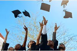 Graduates wearing caps and gowns tossing their mortarboards into a clear blue sky.
