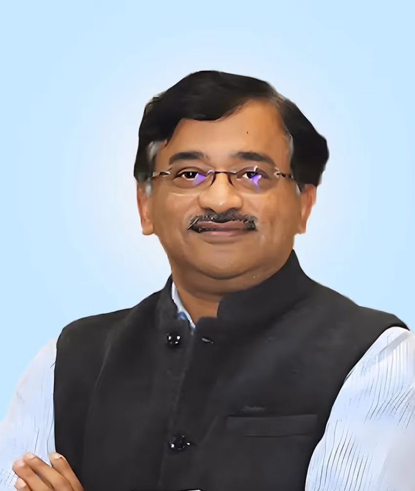 Man wearing glasses and a black sleeveless jacket over a white shirt, smiling with arms crossed against a light blue background.