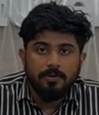 Man with dark hair and beard wearing a black and white striped shirt, looking forward.